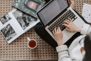 crop young businesswoman using laptop while drinking tea at home